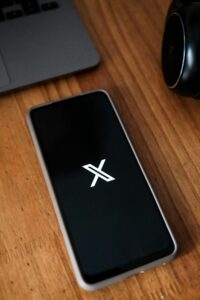 Smartphone displaying a logo on a wooden desk next to a laptop and headphones.